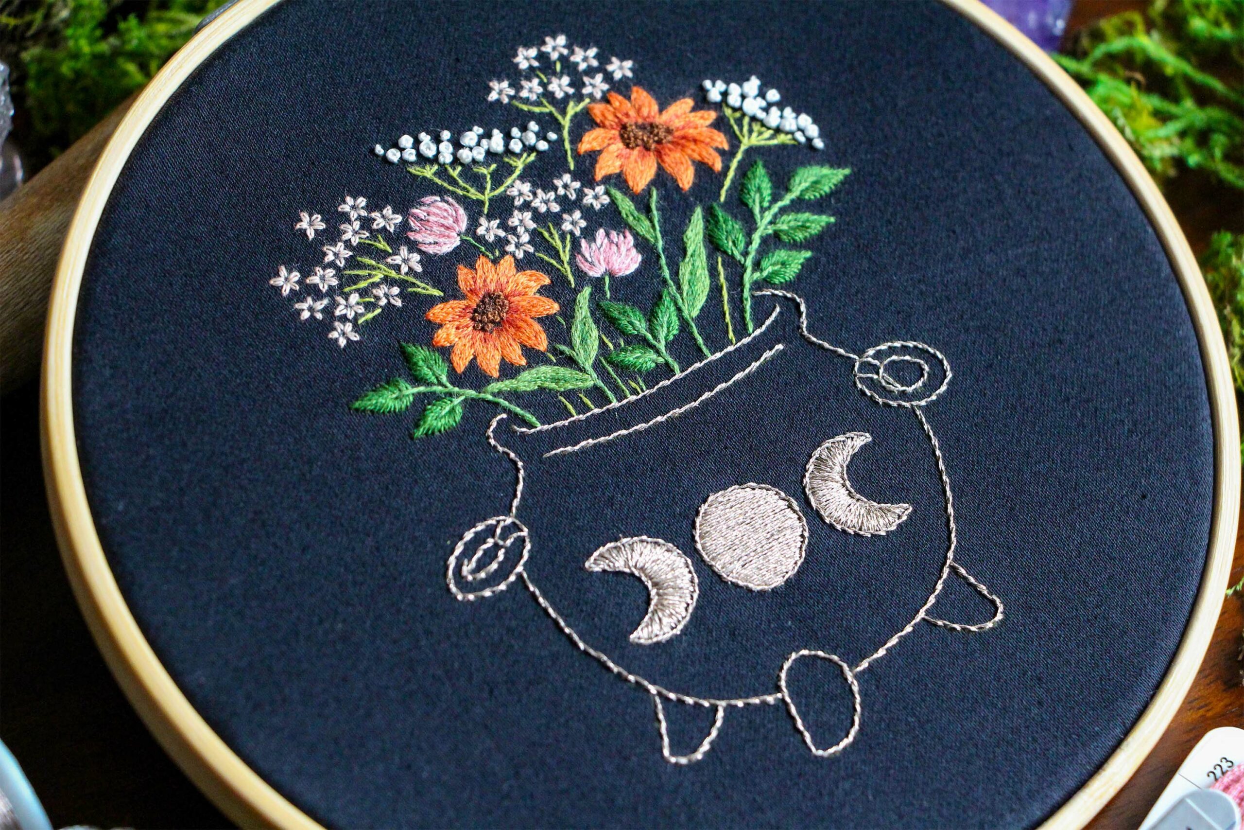 A close up of the Wildflower Cauldron embroidery shows the thread painted flowers bursting out of the embroidered cauldron